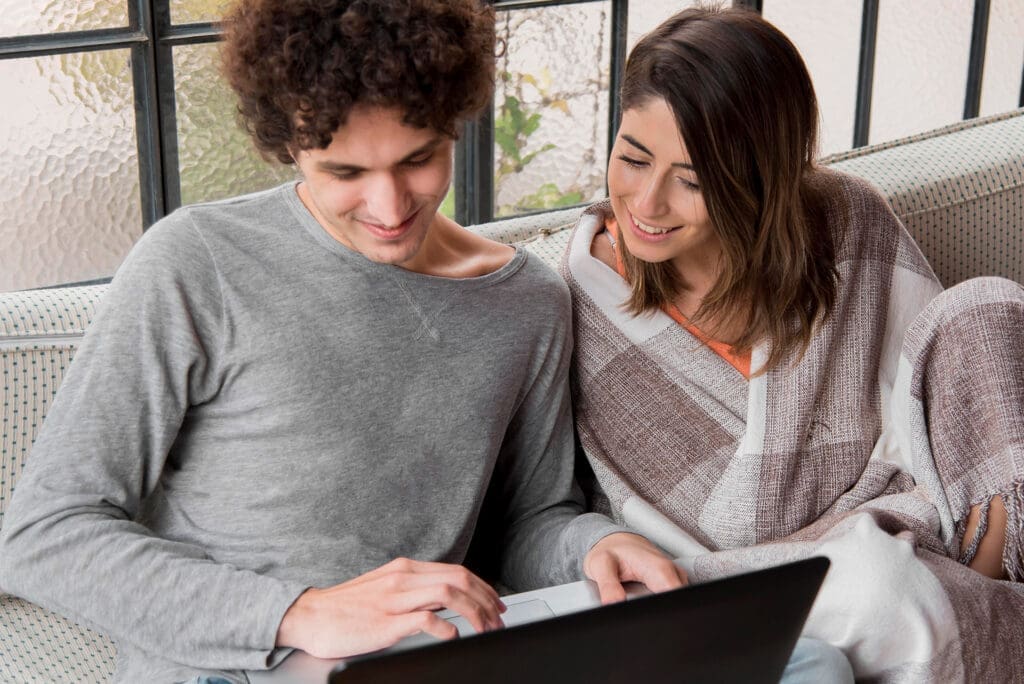 Couple sitting together with a laptop, engaged in discussion and sharing ideas in a cozy indoor setting.